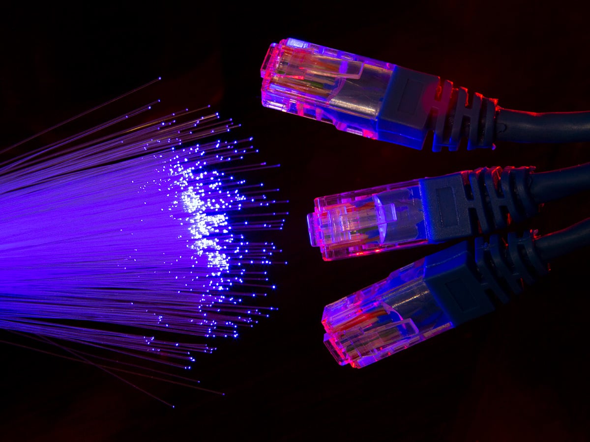 Three Ethernet cables with illuminated red and blue connectors on the right, and a bundle of glowing blue fiber optic strands on the left, set against a dark background